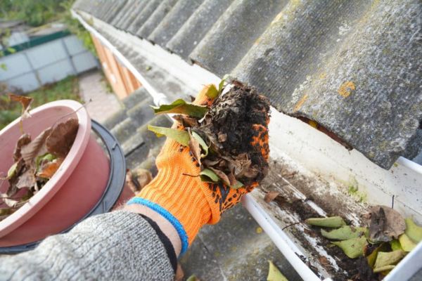 Technician cleaning debris from residential rain gutters during routine maintenance.